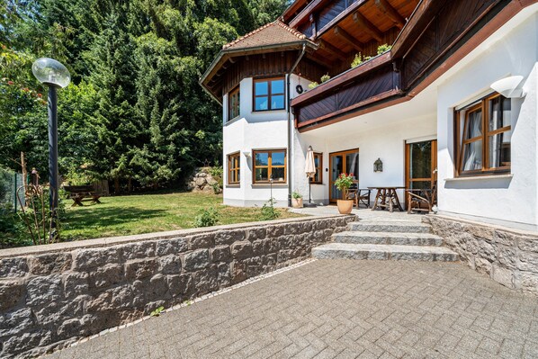 A two-story house with a stone wall, wooden steps, and a garden.