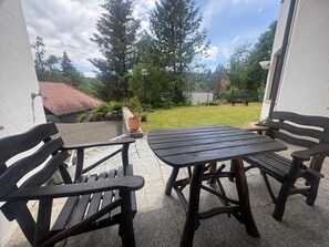 An outdoor patio with a table and two benches, surrounded by a garden and trees. - Apartment 'Auszeit Im Schwarzwald' with Private Terrace, Shared Garden and Wi-Fi (Schonach im Schwarzwald)