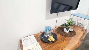 Ein Empfangsschalter mit Fernseher, Holztisch, Willkommenskarte, Wasserflaschen, Gläsern, einer kleinen Pflanze und einer Taschentuchbox.