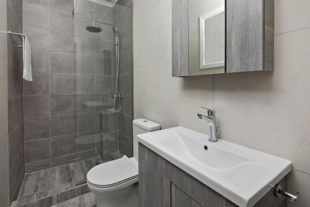 A modern bathroom with a glass-enclosed shower, a white toilet, and a white sink with a mirror above.