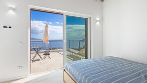 Un dormitorio con cama, una puerta corrediza de vidrio que da a un patio exterior con vista al mar y un techo con vigas de madera a la vista.