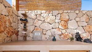 Una pared de piedra con un estante de madera, una pequeña estatua y un enchufe.