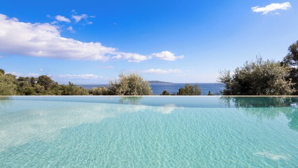 Una piscina infinita transparente con vistas al mar y a la tierra distante.