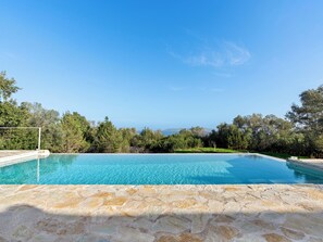 A clear blue pool with a stone deck, surrounded by greenery and trees, under a clear sky. - Villa Thymari, new cocoon of privacy and peace (sivota village)