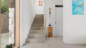 A staircase leading to a room, a stone wall, a door with a painting, and a small table with a bottle. - Villa Thymari, new cocoon of privacy and peace (sivota village)