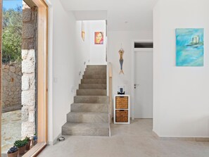 A staircase leading to a room, a stone wall, a door with a painting, and a small table with a bottle. - Villa Thymari, new cocoon of privacy and peace (sivota village)