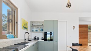 A modern kitchen with a built-in oven, a sink, and a dining area with a wooden table and chairs. - Villa Thymari, new cocoon of privacy and peace (sivota village)