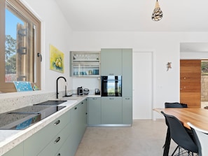 A modern kitchen with a built-in oven, a sink, and a dining area with a wooden table and chairs. - Villa Thymari, new cocoon of privacy and peace (sivota village)