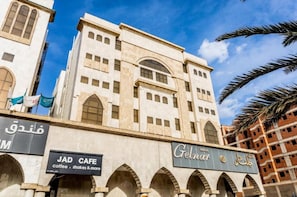Un hôtel avec une entrée en arc de cercle bien visible, une enseigne indiquant un café JAD, et un ciel d’un bleu éclatant.