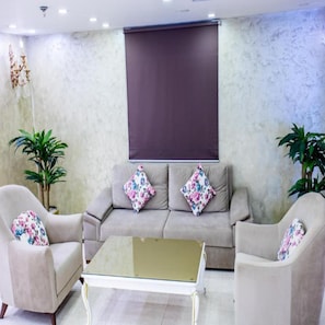 Un salon comprenant un canapé, deux fauteuils, une table basse en verre et deux plantes en pot.