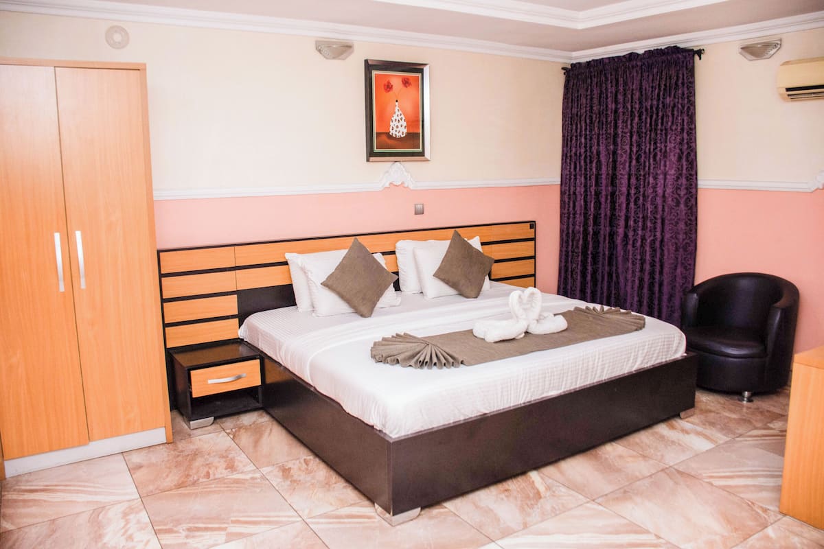 A bedroom with a large bed, a wardrobe, a chair, and a framed picture on the wall.