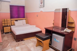 Un dormitorio con cama, mesita de noche, cómoda, espejo y un refrigerador pequeño.