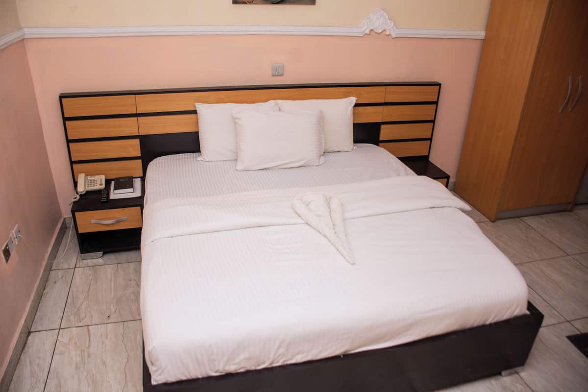 A neatly made double bed with a wooden headboard, a bedside table with a phone and a book, and a wardrobe to the right.