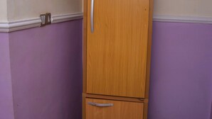 Ein Eckzimmer mit einem Holzkabinett, einer violetten Wand, einer kleinen Mülltonne und einer Streifenmatte.
