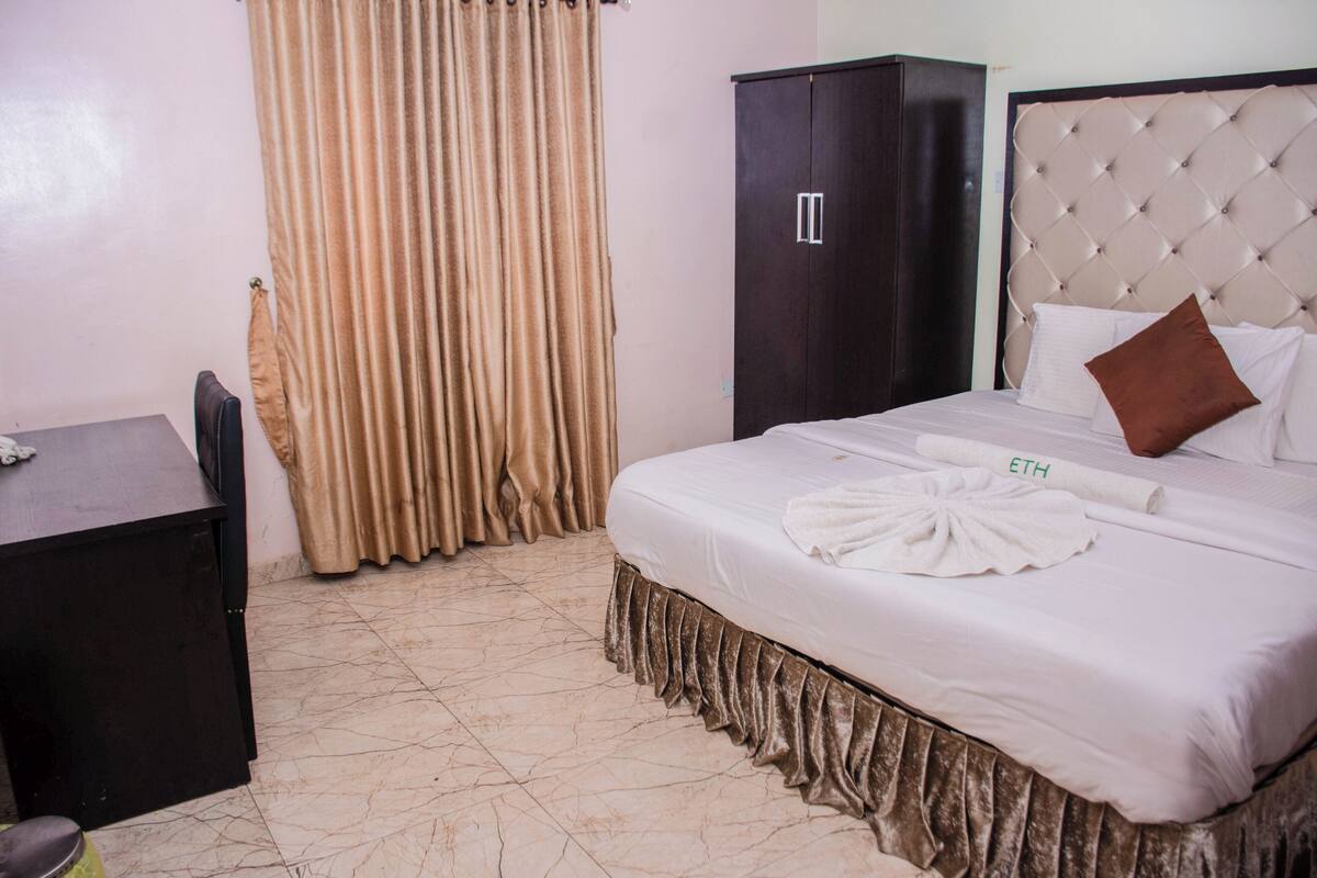 A hotel room with a bed, a wardrobe, a desk, and a curtain.