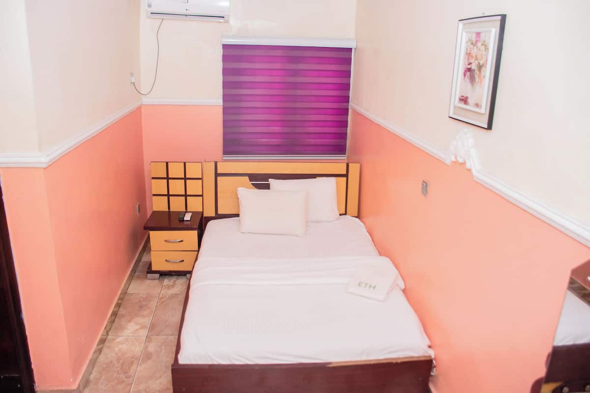 A small, neatly arranged bedroom with a bed, bedside table, and a wall-mounted air conditioning unit.