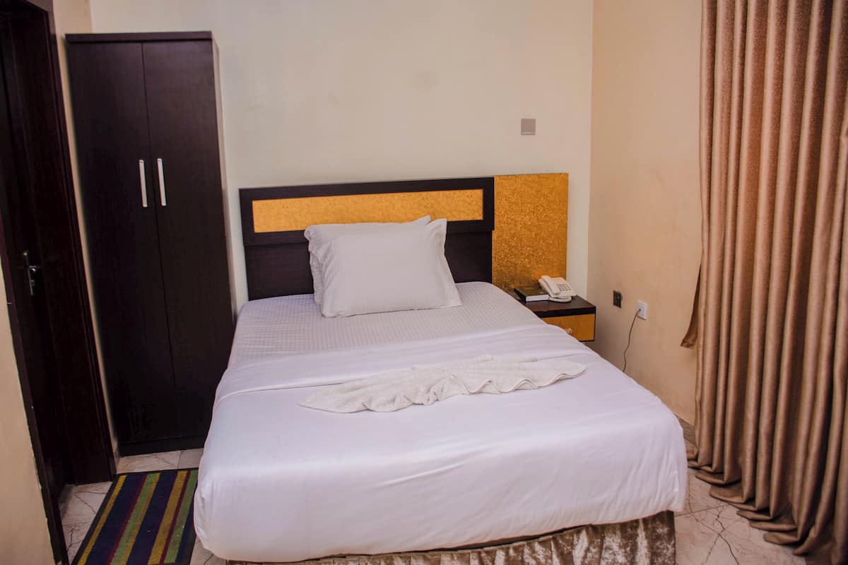 A hotel room with a bed, a wardrobe, a telephone, and a curtain.