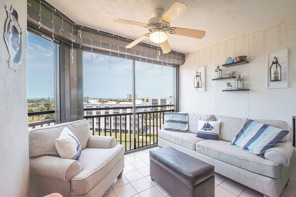 En balkon med ventilator, sofa, sofabord og udsigt til bybilledet.