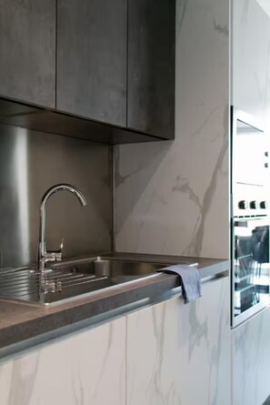 Eine moderne Küche mit einer Edelstahl-Spüle, einer Marmor-Spritzschutzwand und einem eingebauten Backofen.