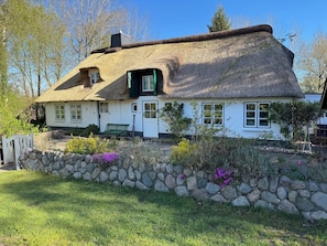 A traditional thatched-roof house with a stone wall and a bench in the garden.