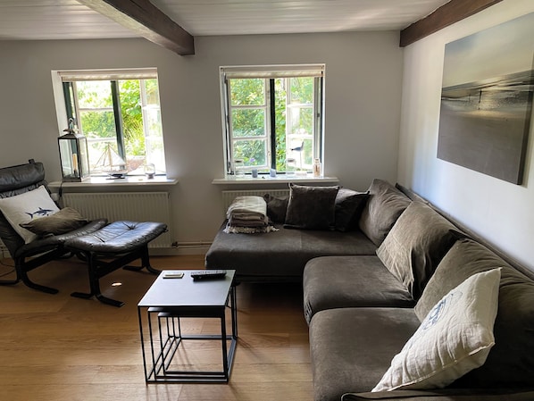 A living room with a leather chair, a sofa, a small table, and two windows with blinds.