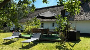 Een rieten dakgebouw met een klein terras, twee loungesteunen, een houten bank en een beschaduwd gedeelte.