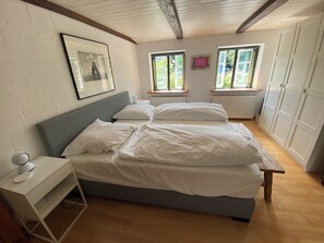 A bedroom with a bed, bedside table, and a window with a view of greenery.