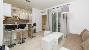 A modern kitchen with bar stools, a dining table, and a sofa in a bright living area with a sliding glass door.