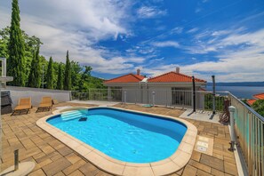 Ein Swimmingpool mit Liegestühlen, Blick auf ein rotes Haus und ein klarer Himmel.