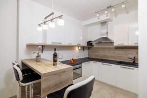 Eine moderne Küche mit weißen Schränken, einer Holzinsel, Barhocker, Pendelleuchten und einem eingebauten Ofen.
