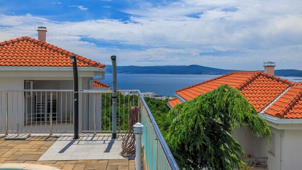 A residential building with a tiled roof, a balcony, and a view of the sea.
