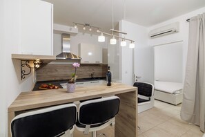 Eine moderne Küche mit Holztischplatte, zwei schwarzen Stühlen, einem kleinen Tisch mit Blumenvase und einer Hängelampe.