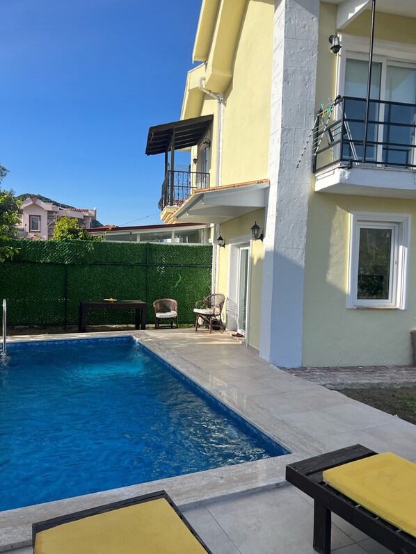 A swimming pool with a patio area, a small table, and two chairs.