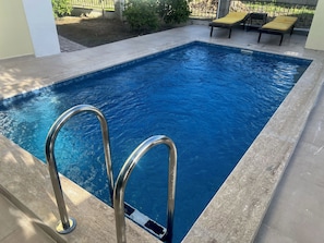 Une piscine rectangulaire dotĂ©e de rampes mĂ©talliques et entourĂ©e dâune terrasse carrelĂ©e.