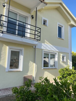 A two-story building with multiple windows, a balcony with a railing, and a small garden area.