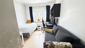 A modern hotel room with a bed, a sofa, a desk with a computer, a TV, and a window with curtains. - Stylish apartment in the heart of Reykjavík, Vesturbær (Reykjavík)