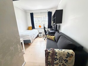 Ein modernes Hotelzimmer mit Bett, einer Sitzecke, einem Schreibtisch mit Computer, einem Fernseher und einem Fenster mit Vorhängen.