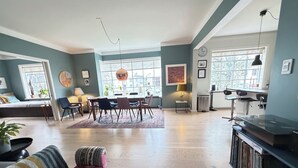 A spacious living area with a dining table, chairs, a sofa, a bookshelf, and a large window providing natural light. - Stylish apartment in the heart of Reykjavík, Vesturbær (Reykjavík)