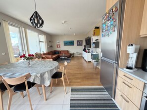 Et moderne køkken med køleskab, kaffemaskine og spiseplads med bord og stole.