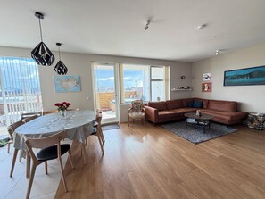 Ein großzügiger Wohnbereich mit Esstisch, Sofa und großen Fenstern, die einen Blick auf die Stadt bieten.