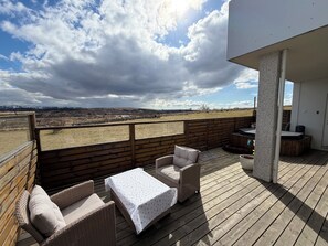 En træterrasse med fletningsmøbler og et bord, med udsigt over et landskab med fjerne bakker.