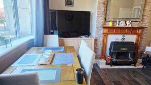 Een woonkamer met een open haard, televisie en een eethoek met plaatsmatten.