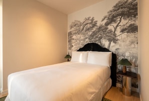 A neatly made bed with white linens in a room with a large wall mural of trees. - Be Mate Chamberí - Temporary Stays (Madrid)