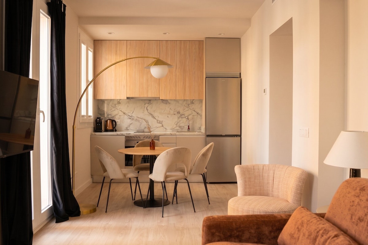 A modern kitchen with a marble backsplash, a dining area with a round table and chairs, and a living area with a sofa and a lamp.