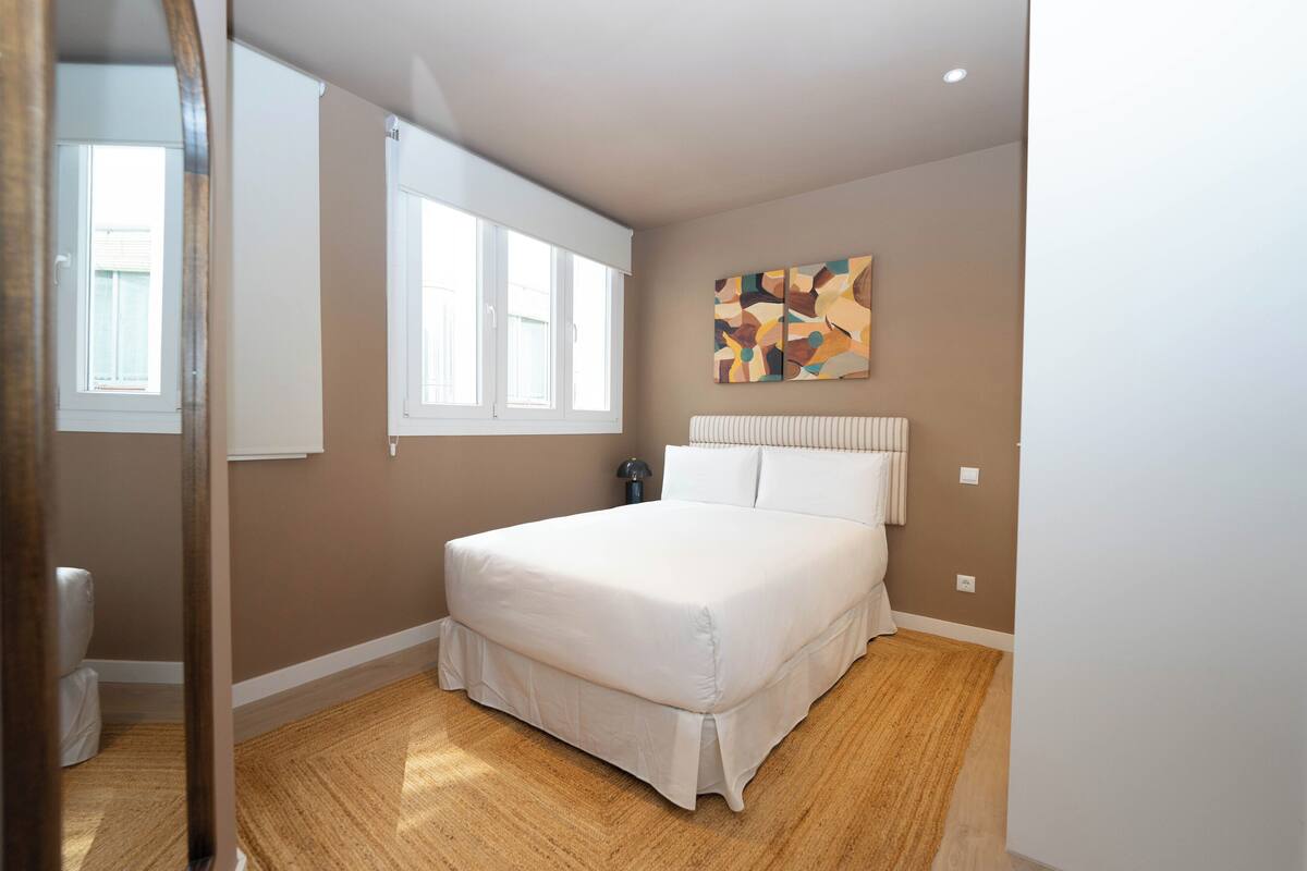 A bedroom with a large bed, a window, a radiator, and a wall-mounted artwork.