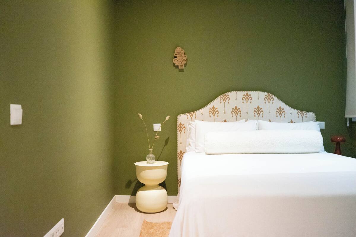 A bedroom with a bed, a nightstand, and a wall-mounted light fixture.