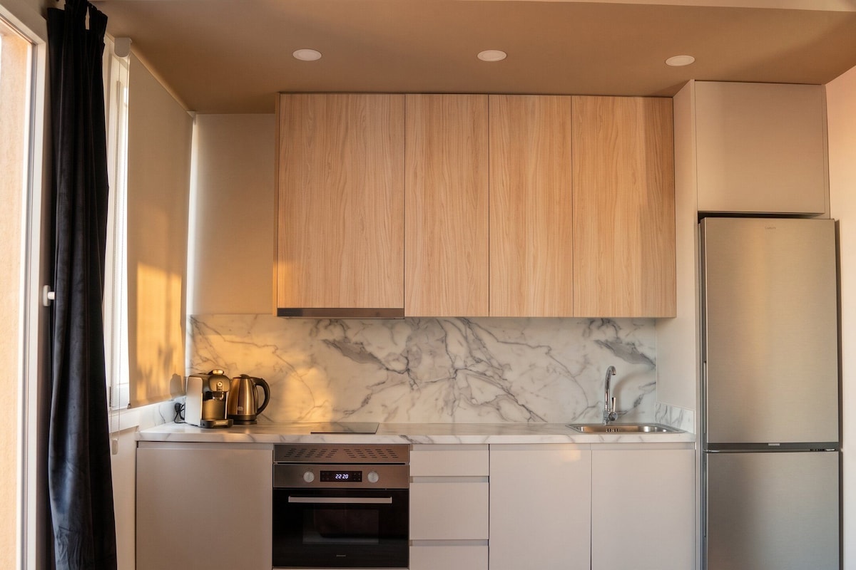 A compact kitchen with a built-in oven, a stainless steel refrigerator, and a marble backsplash.