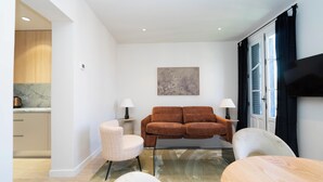 A modern living room with a sofa, two chairs, a dining table, and a kitchen area visible through an open door. - Be Mate Chamberí - Temporary Stays (Madrid)