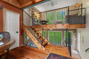 Un escalier en bois à plusieurs niveaux, doté d’une rampe, un coin repas avec une table et des chaises, et une vue sur la verdure environnante.
