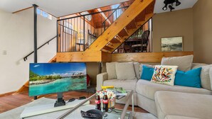 Een woonkamer met een bank, een salontafel, een televisie en een trap.
